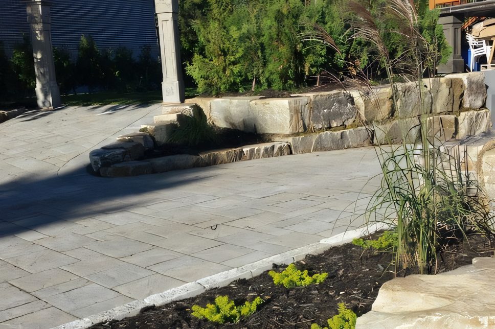 Muret de pierre naturelle le long d’une entrée de pavé, gazon en avant