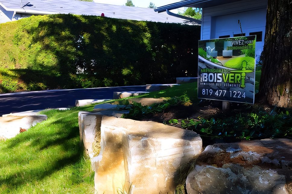 L’enseigne de chantier d’Aménagement Paul Boisvert devant une grosse pierre et une pelouse