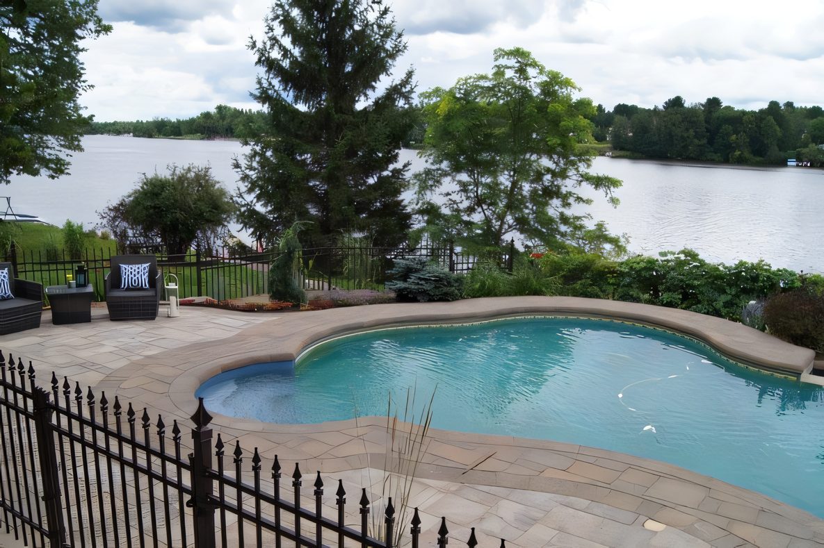 Piscine creusée au bord d’un lac, terrasse de pavé, clôture noire