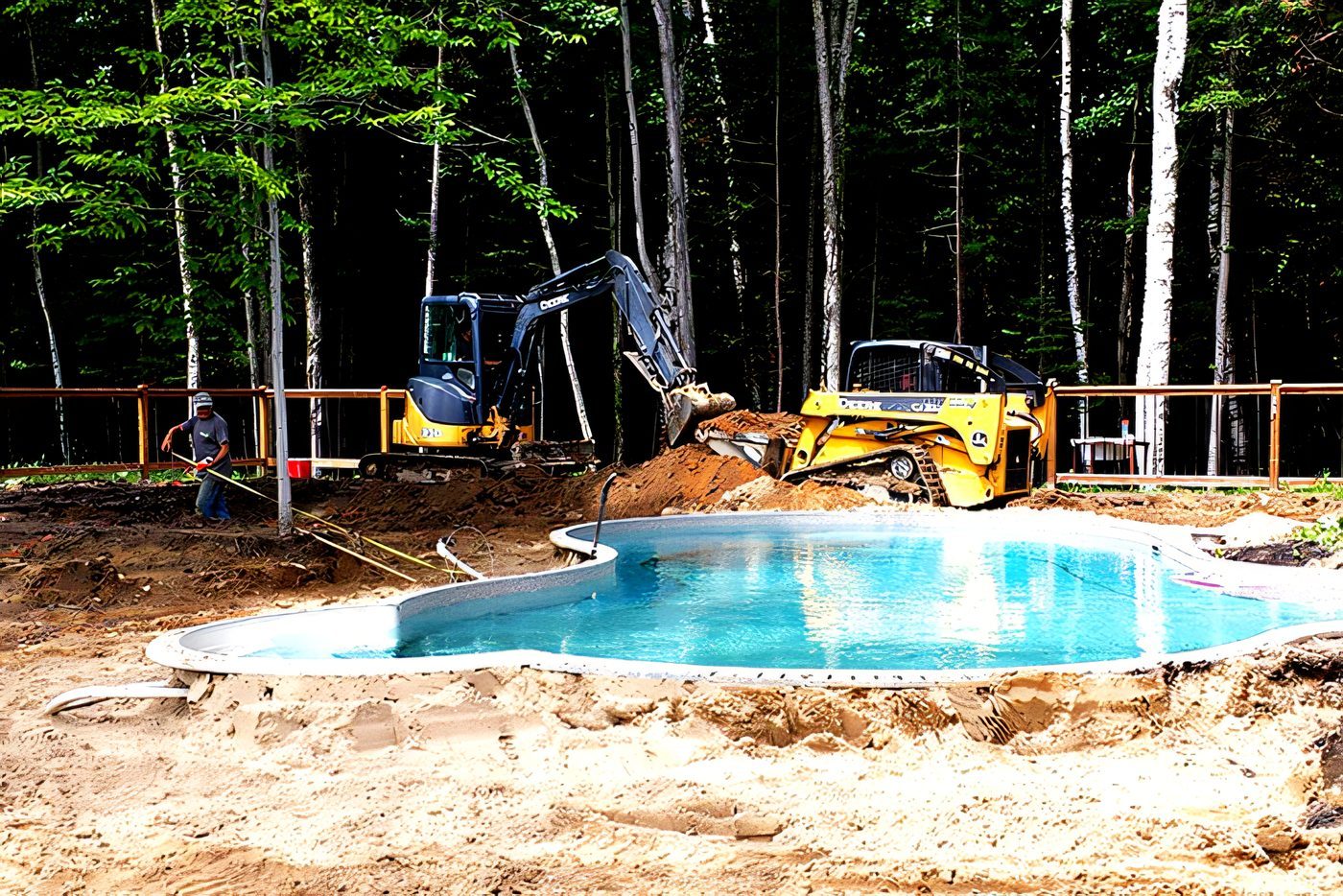 Excavation d’une piscine creusée au fond d’un terrain boisé, la pelle chenillée à côté du bassin